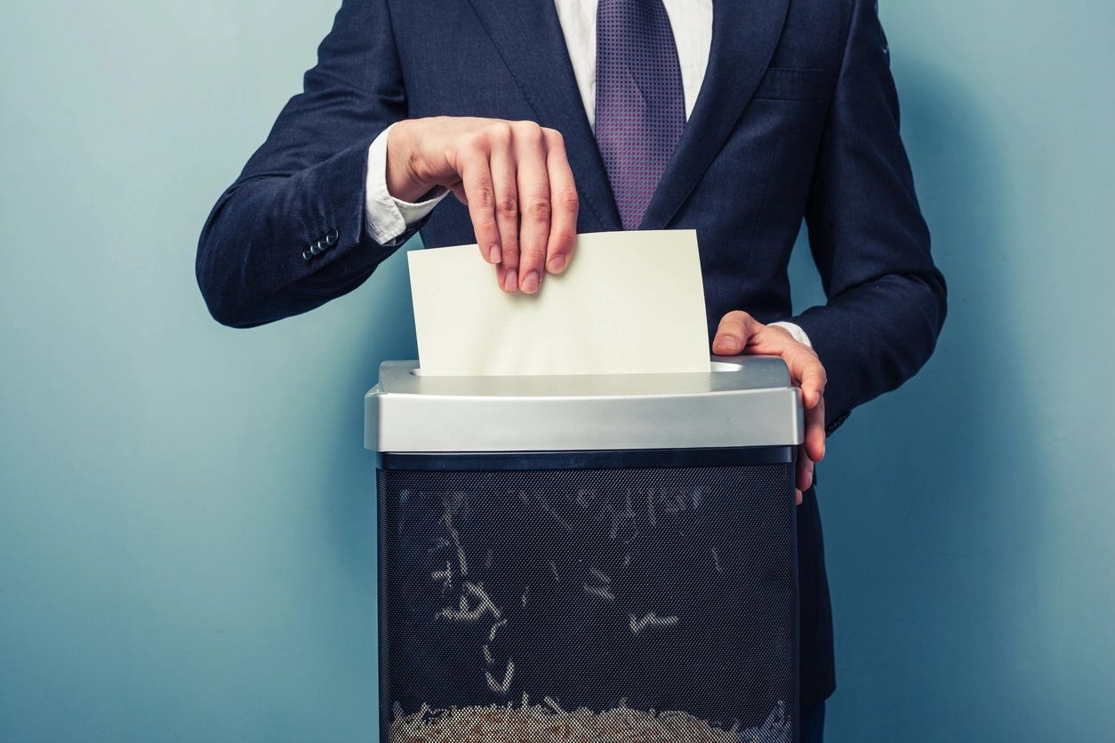 A man in a suit and tie putting papers into a shredder.